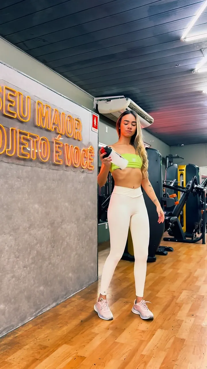 Atleta com coqueteleira na academia, ao lado do letreiro em neon “Seu maior projeto é você”
